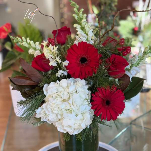 Red gerbera daisies and roses with white hydrangea in a glass vase