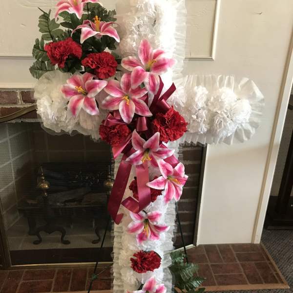 Standing floral cross with pink lilies, red carnations, and white ruffles