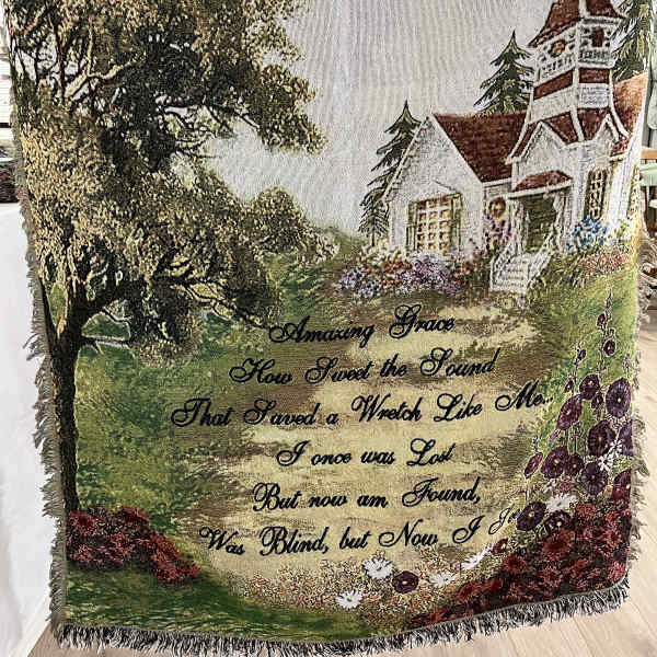 Decorative woven throw with a house, trees, and floral border