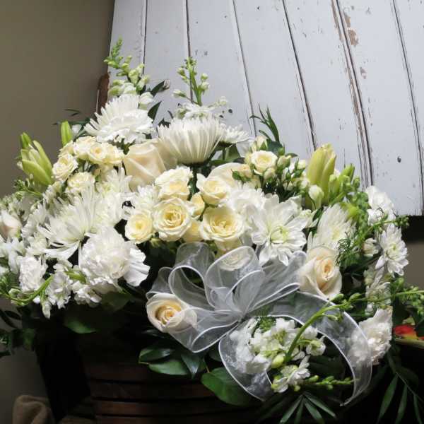 White floral arrangement with roses, daisies, and lilies in a basket
