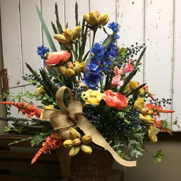 Colorful mixed flower arrangement in a woven basket with a burlap ribbon