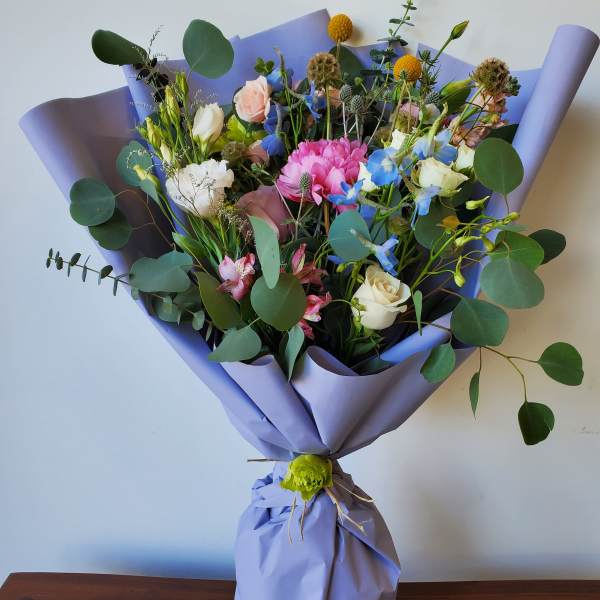 Mixed bouquet of pastel flowers wrapped in lavender paper
