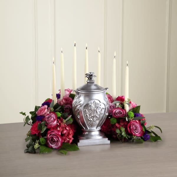 Pink rose arrangement with tall white candles around a silver urn