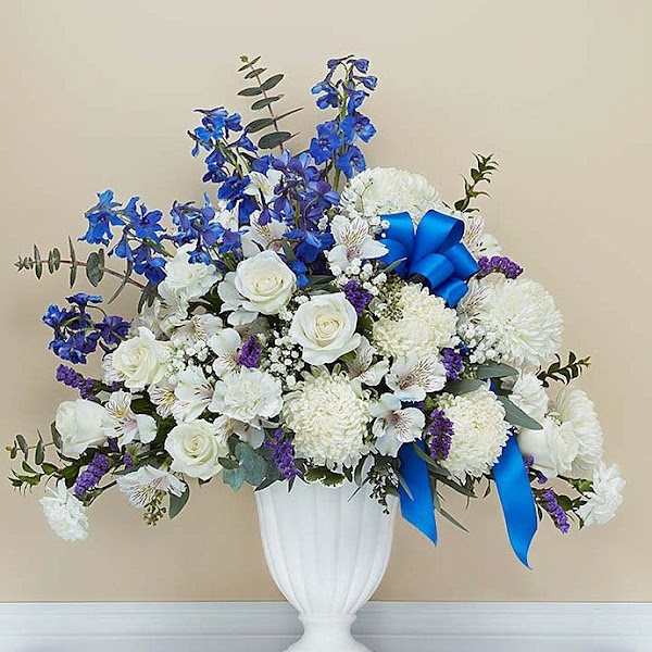 White and blue floral arrangement in a white vase with ribbon