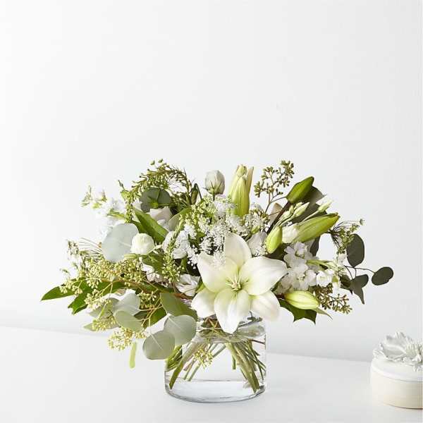 White lilies and mixed white flowers in a clear glass vase