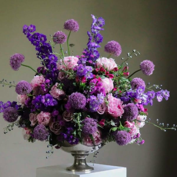 Large purple and pink floral arrangement in a silver pedestal vase
