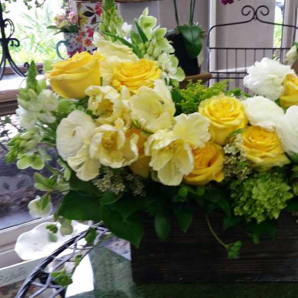 Yellow and white roses arranged in a dark rectangular container
