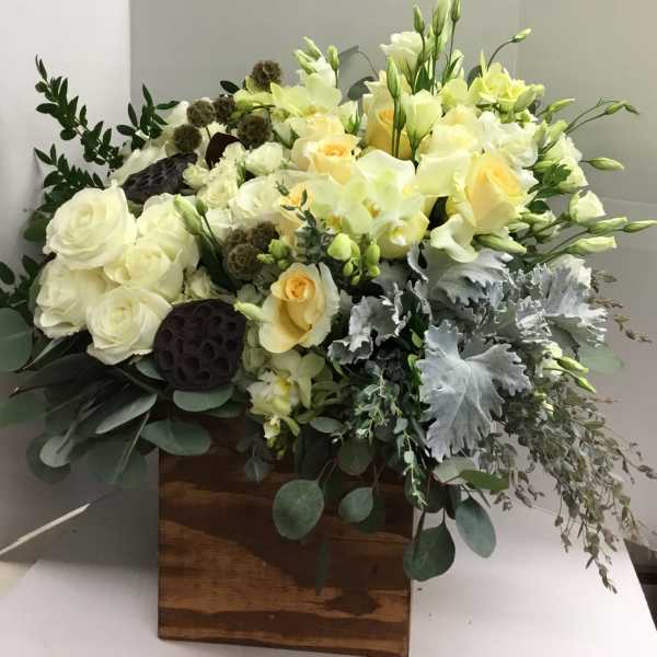 White and pale yellow floral arrangement in a wooden box with greenery