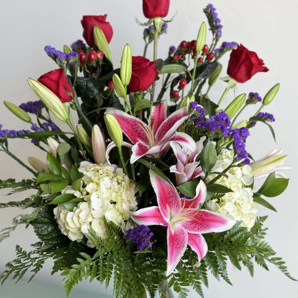 Bouquet of pink lilies, red roses, and white hydrangeas in a glass vase