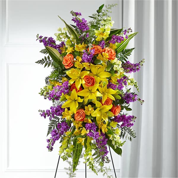 Tall standing floral spray with yellow lilies, orange roses, and purple flowers