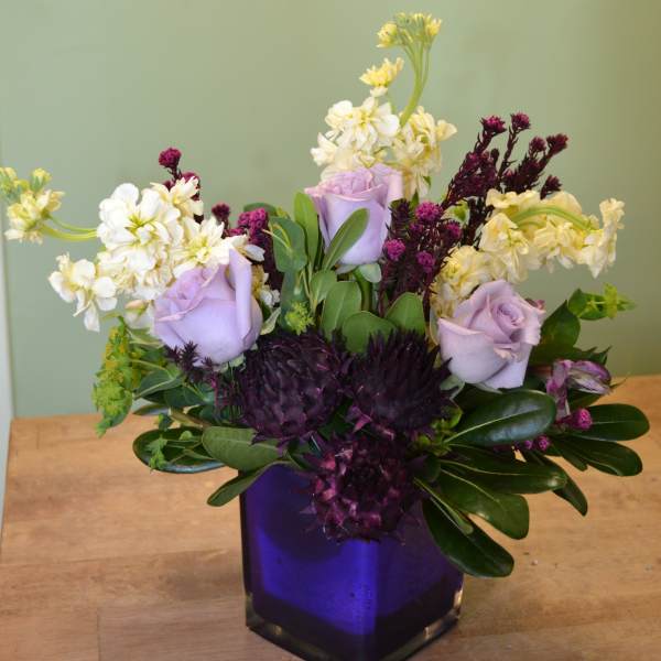 Lavender roses and white flowers in a purple glass vase