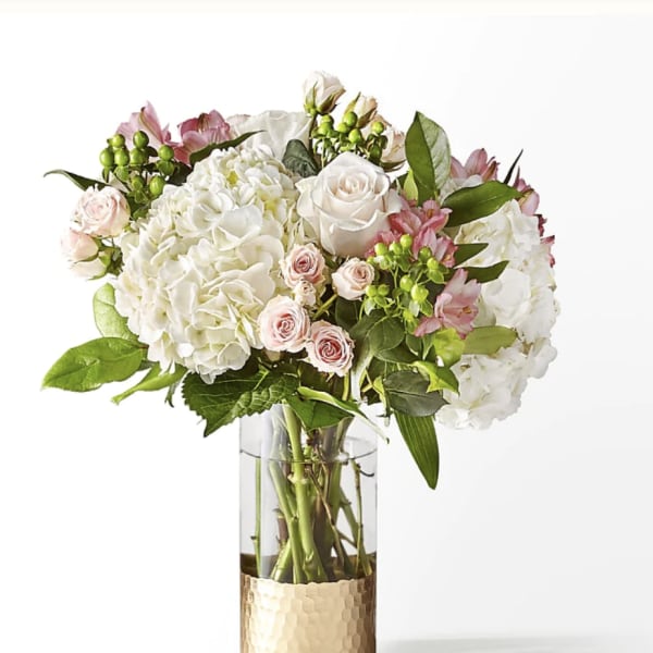White and blush bouquet in a clear glass vase with a gold base