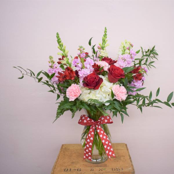 Mixed bouquet of red roses, pink carnations, and white hydrangeas in a glass vase