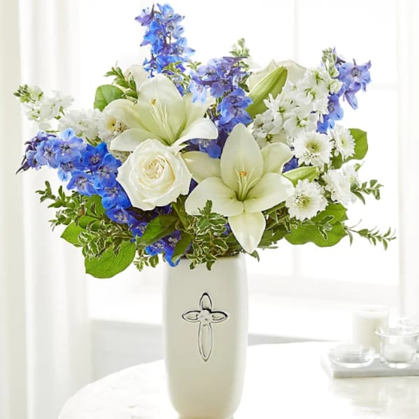 White lilies, roses, and blue flowers in a white vase with a silver cross design