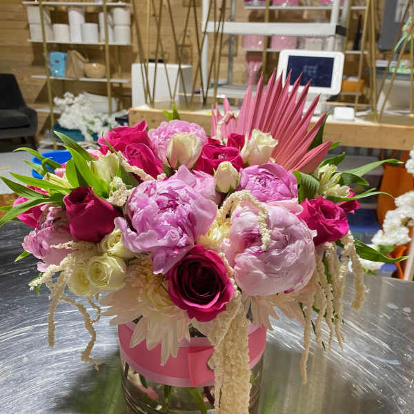 Low pink and white arrangement with peonies and roses in a glass vase wrapped with pink ribbon