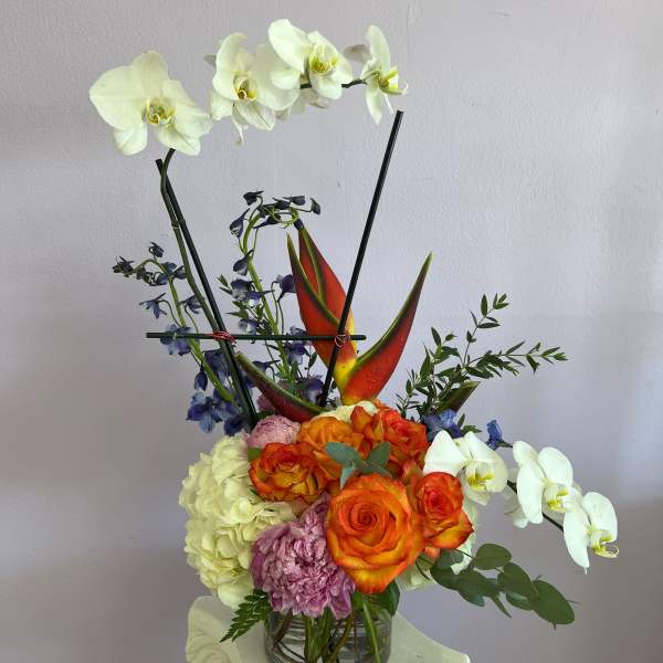 Mixed floral arrangement with white orchids and orange roses in a glass vase