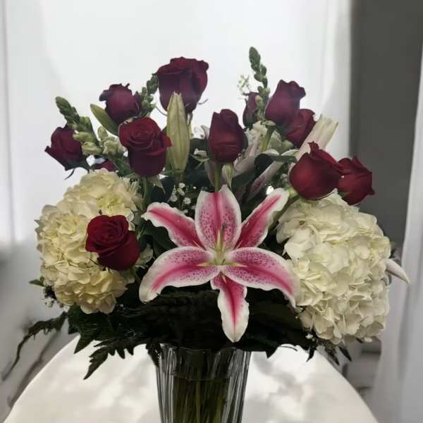 Bouquet of red roses, white hydrangeas, and a pink lily in a glass vase