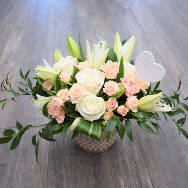 Low floral arrangement of white roses, lilies, and peach spray roses in a patterned vase