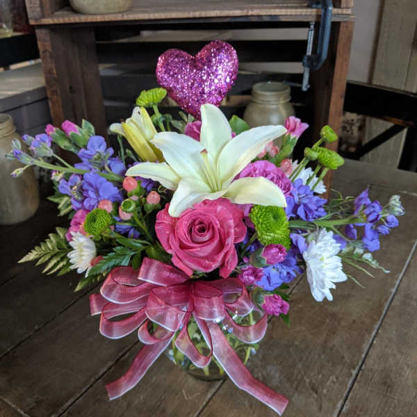 Bouquet of pink roses, white lilies, and purple flowers with a glitter heart pick