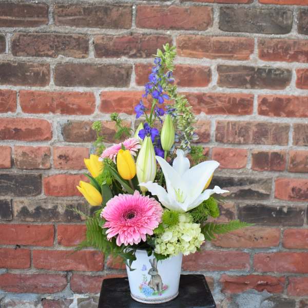 Mixed bouquet in a white vase with pink gerbera daisies, yellow tulips, and a white lily
