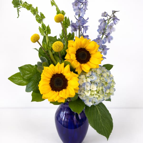 Sunny bouquet with sunflowers, blue hydrangea, delphinium and Bells of Ireland in a cobalt glass vase