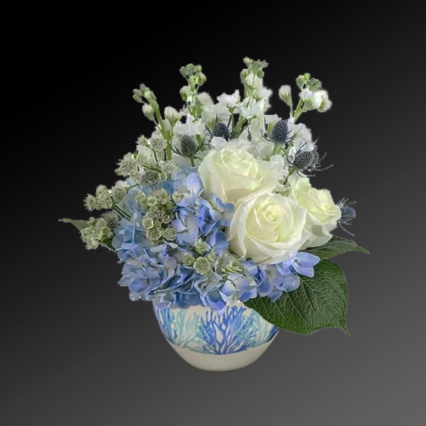 White roses and blue hydrangeas in a patterned ceramic vase
