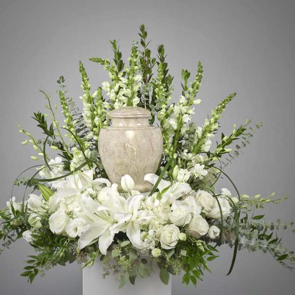 White lilies and roses arranged around a stone urn with tall white snapdragons behind.