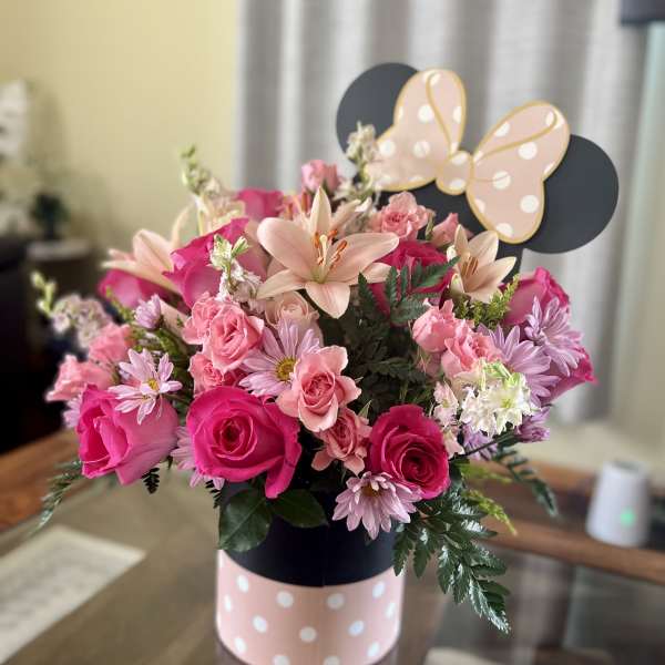 Pink and peach flower arrangement in a polka-dot box with a butterfly topper