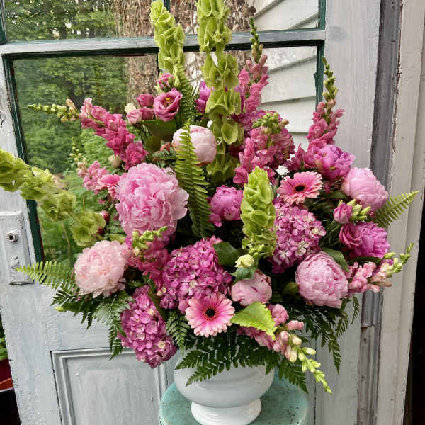 Pink floral arrangement in a white urn vase with tall green spikes