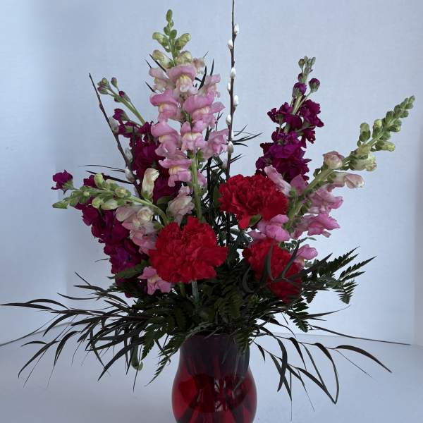 Tall mixed bouquet of pink and red flowers in a red glass vase