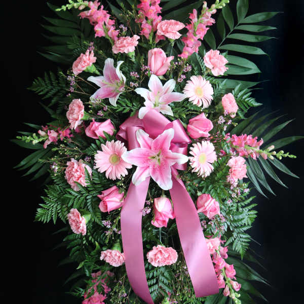 Pink floral standing spray with lilies, roses, and carnations on a ribboned easel