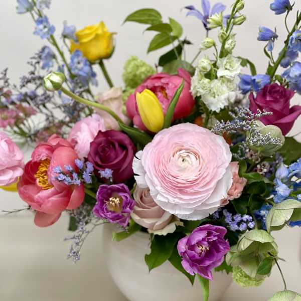 Mixed bouquet of pink, purple, yellow, and blue flowers in a white vase