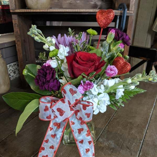 Mixed bouquet with a red rose and heart ribbon in a glass vase