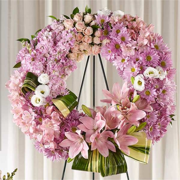 Pink floral wreath on a black stand with lilies and daisies