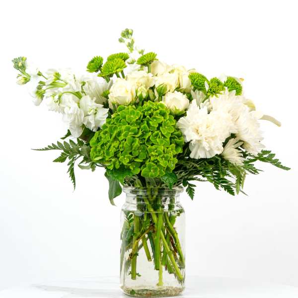 White and green mixed flower arrangement in a clear glass jar vase