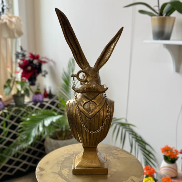 Gold rabbit bust sculpture with tall ears and a mustache on a pedestal