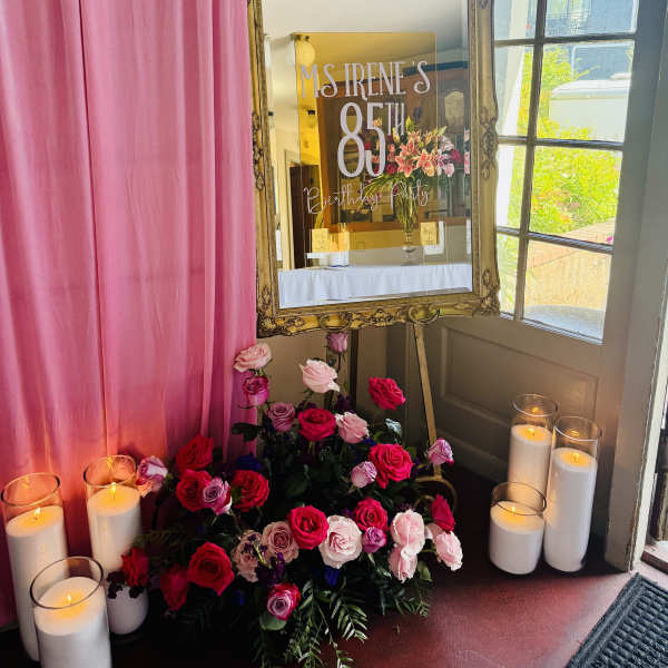 Pink and red rose arrangement with candles beside an ornate mirror sign