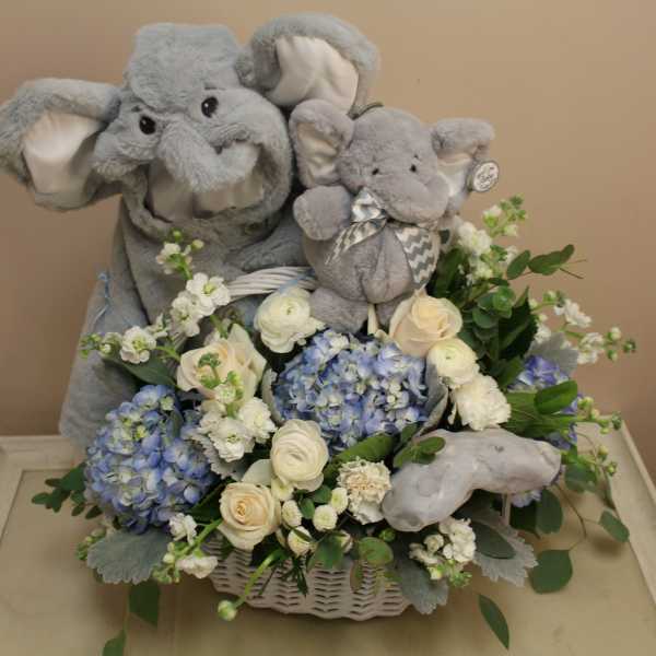 Two gray plush elephants in a basket with blue and white flowers