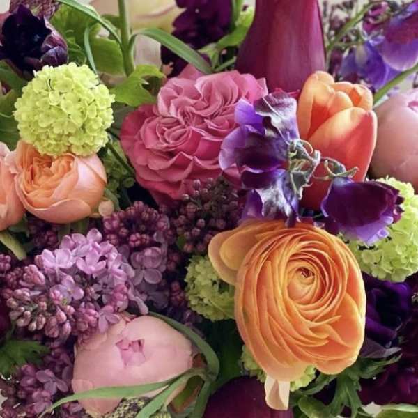 Vibrant mixed arrangement with pink roses, orange ranunculus, tulips, and purple blooms.