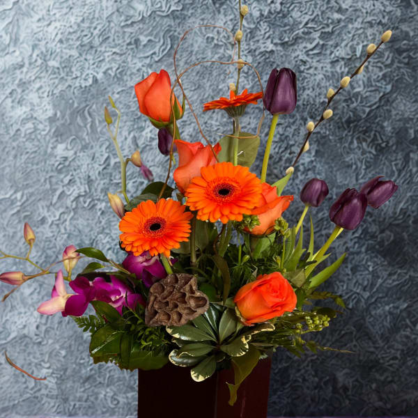 Orange and purple floral arrangement in a dark square vase