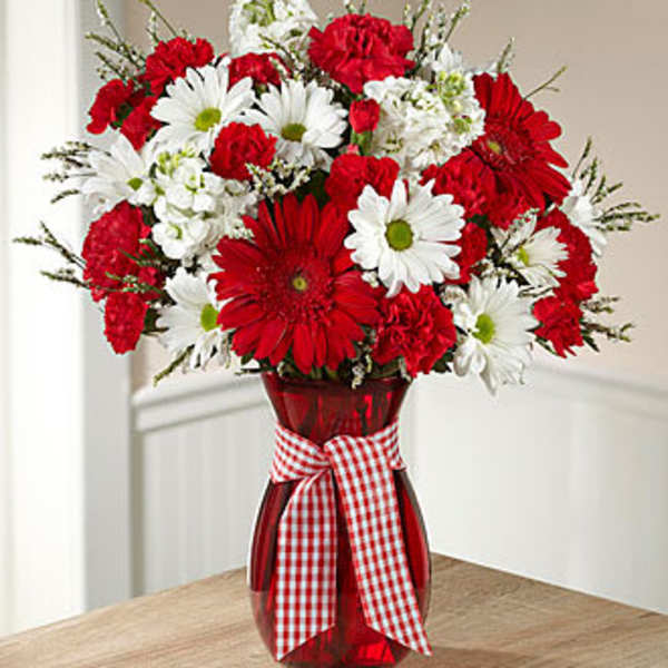 Red and white daisy bouquet in a red vase with a gingham ribbon