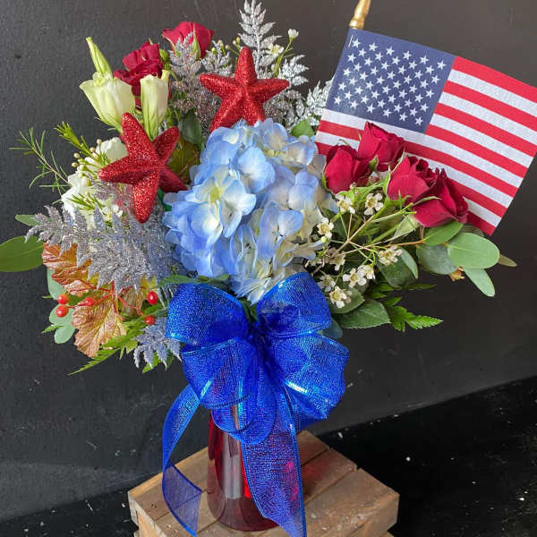 Red, white, and blue floral arrangement with an American flag and blue ribbon