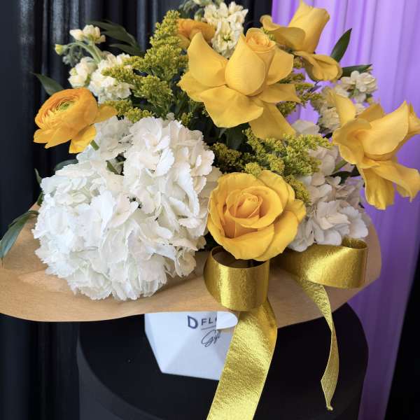 Yellow roses and white hydrangeas in a wrapped bouquet with gold ribbon