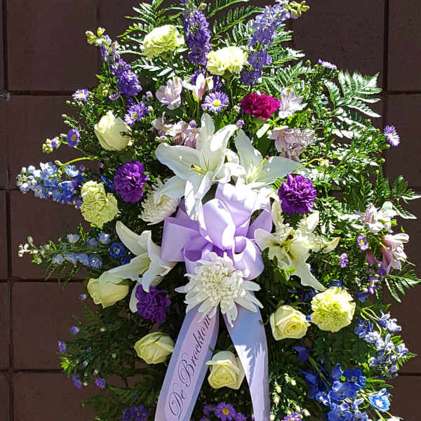 Standing floral spray with white lilies, purple and blue flowers, and a lavender ribbon
