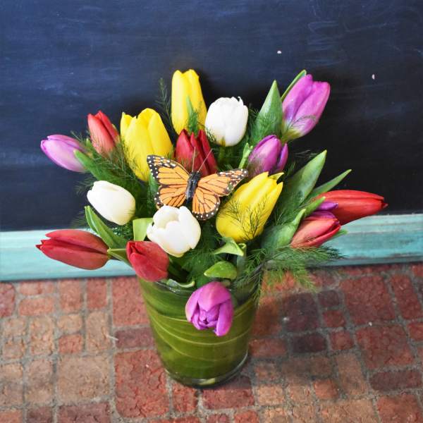 Colorful tulip bouquet in a green glass vase with a butterfly accent