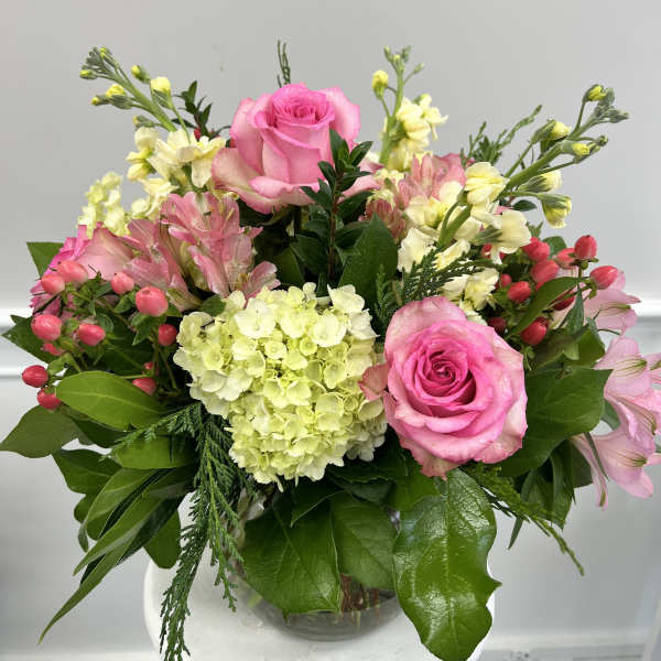 Compact arrangement of pink roses, hydrangea, and mixed pastel blooms in a clear glass vase