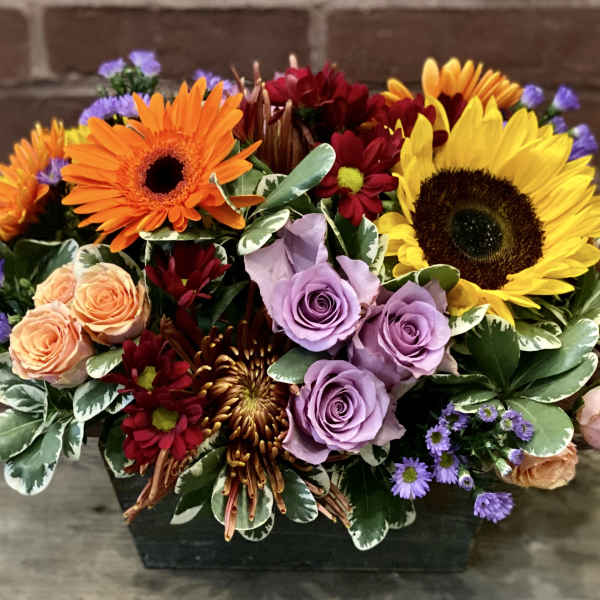 Mixed bouquet with sunflowers, roses, and gerbera daisies in a dark container