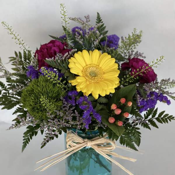 Mixed bouquet with a yellow gerbera daisy in a blue glass vase