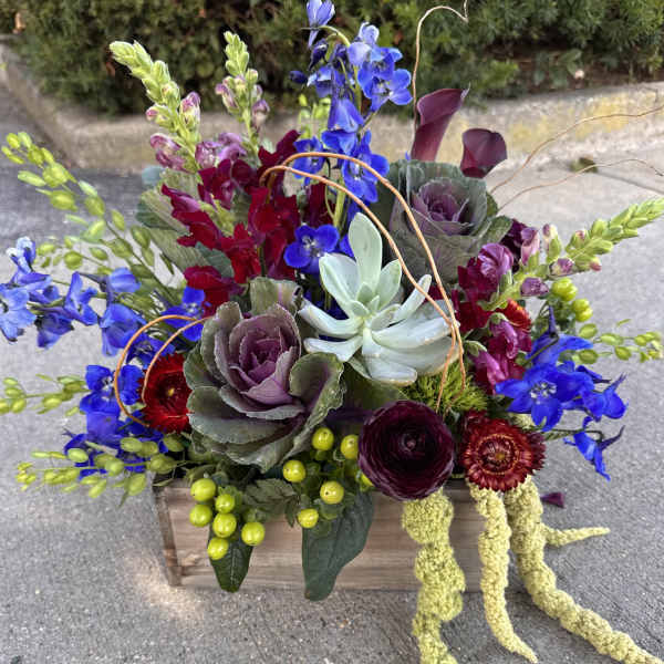 Colorful floral arrangement in a wooden box with blue, burgundy, and purple blooms