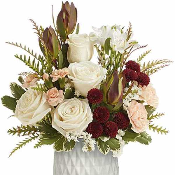 White roses, burgundy blooms, and peach flowers in a white vase